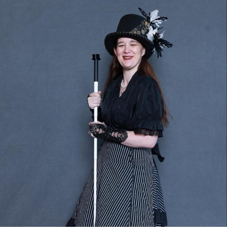 Amy sporting her favorite feathered top hat, wearing black lace gloves, and holder her white cane.